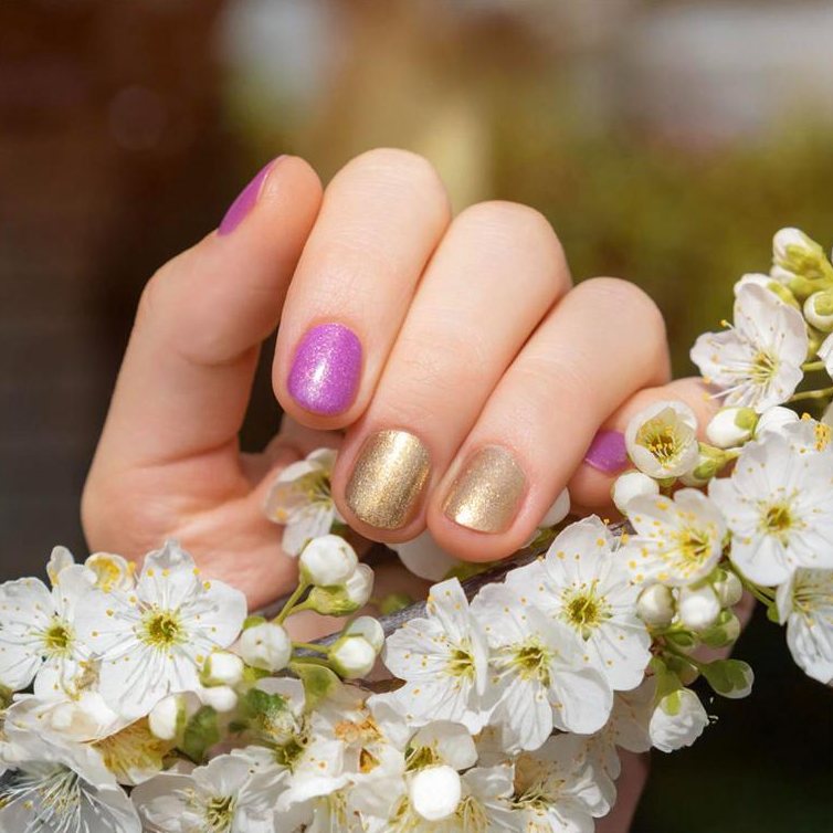 Gold and violet manicure held against white blossoms